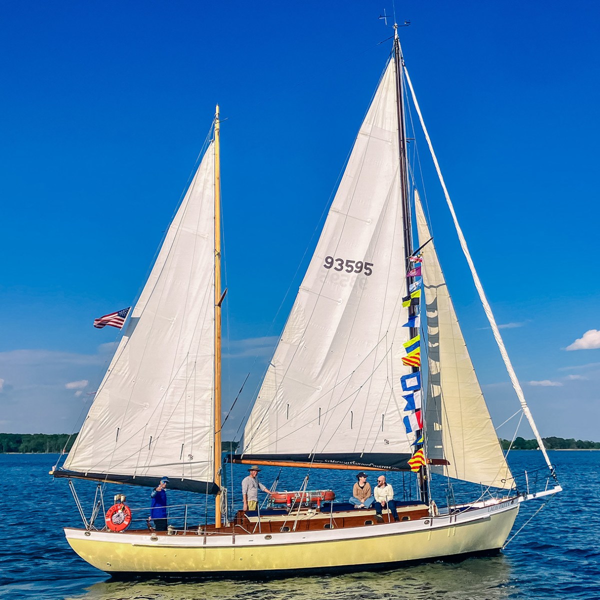 Sailboat with four people on calm water under a clear blue sky.