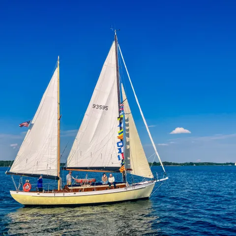 Sailboat with two sails on calm blue water under a clear sky.