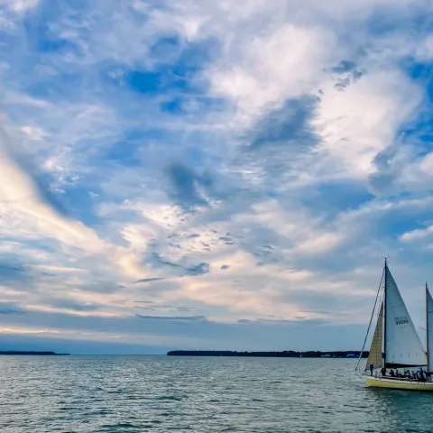 Sailboat on calm water with a dramatic cloudy sky at sunset.