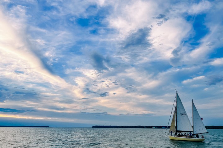 Sailboat on calm water with a dramatic cloudy sky at sunset.