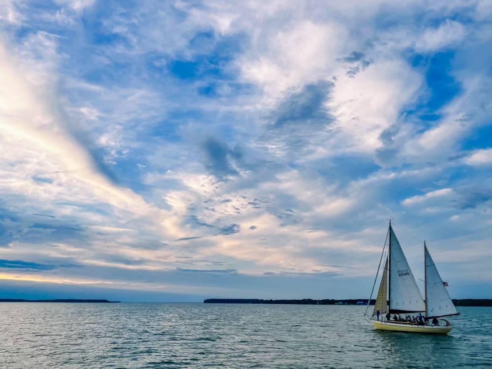 Sailboat on calm water with a dramatic cloudy sky at sunset.