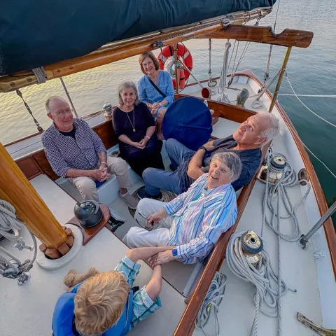 Six adults and a child sitting on a sailboat deck near a marina.