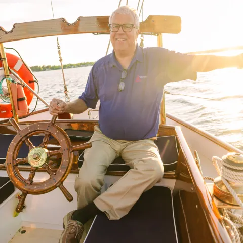 Person steering a boat at sunset, wearing a blue shirt, holding the wheel.