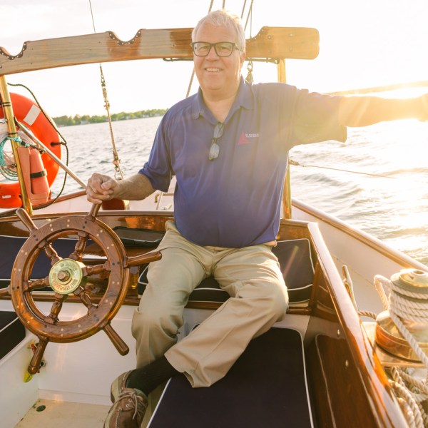 Person steering a boat at sunset, wearing a blue shirt, holding the wheel.