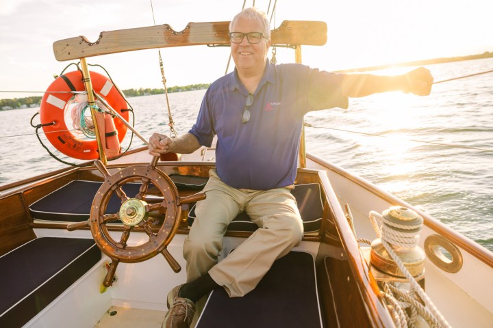 Person steering a boat at sunset, wearing a blue shirt, holding the wheel.