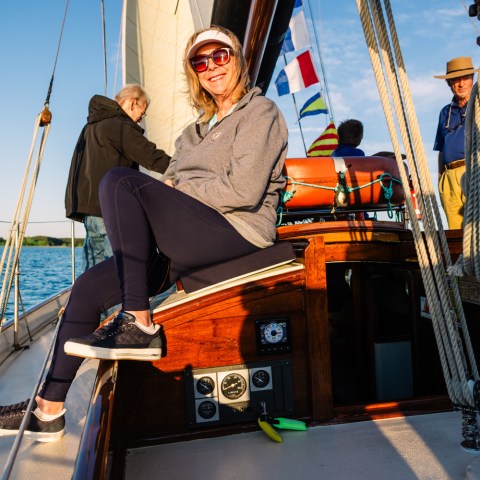 Woman smiling on sailboat deck with two other people on a sunny day.