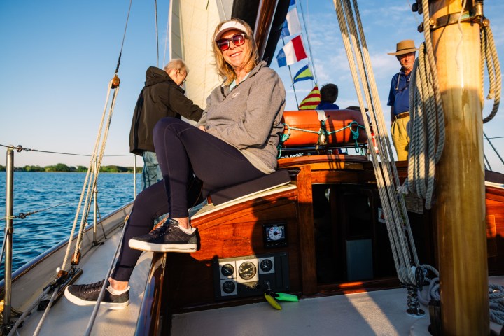 Woman smiling on sailboat deck with two other people on a sunny day.