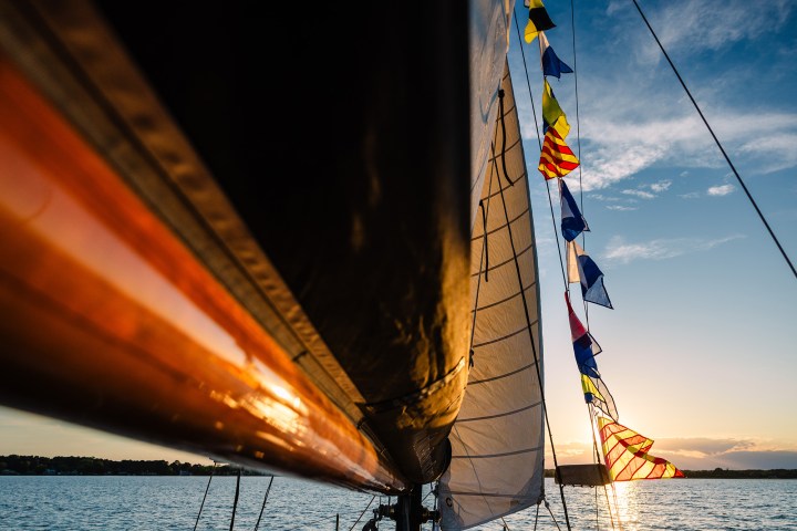 Sailboat with colorful flags at sunset on calm water.