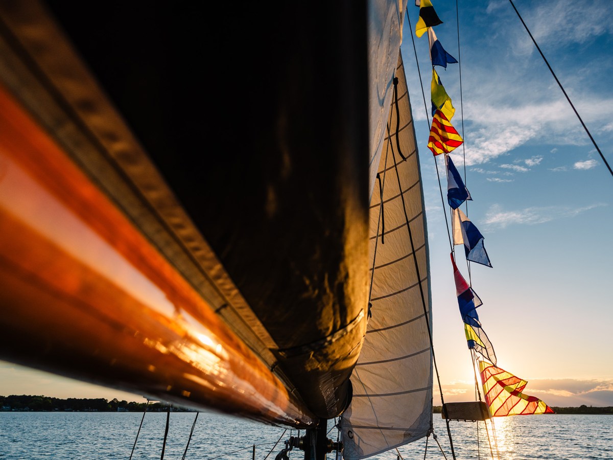 Sailboat with colorful flags at sunset on calm water.