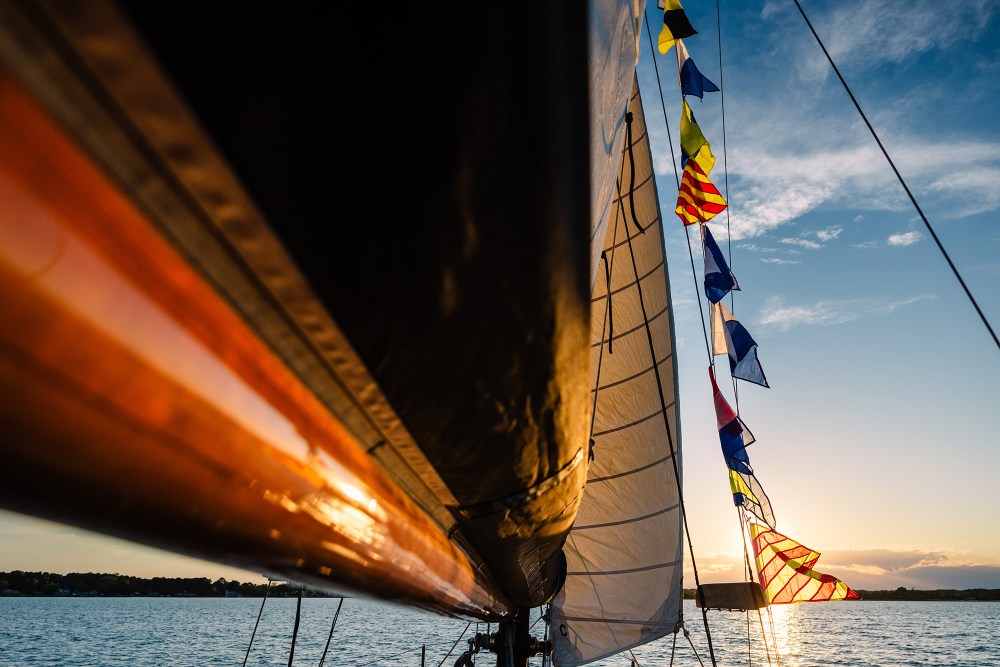 Sailboat with colorful flags at sunset on calm water.
