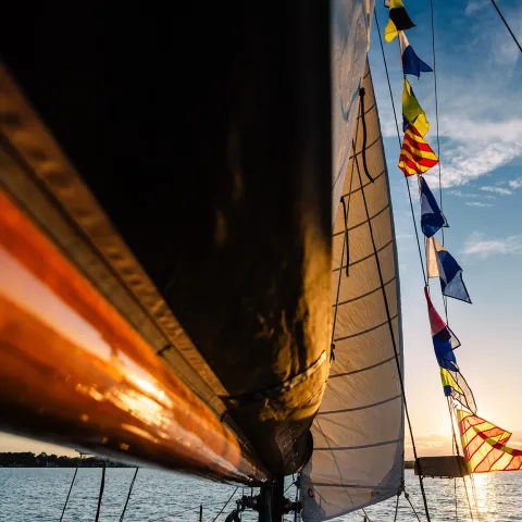 Sailboat mast with colorful flags at sunset on a calm sea.