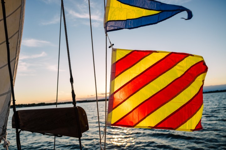 Sailboat flags with red and yellow stripes against a sunset on the water.