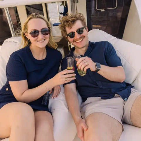 Couple in sunglasses toasting drinks on a boat.