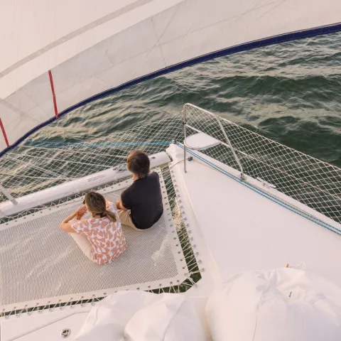 Two people sitting on a sailboat's deck over water.