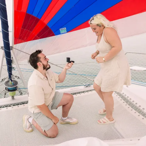 Person kneeling and proposing on a sailboat under a colorful sail.