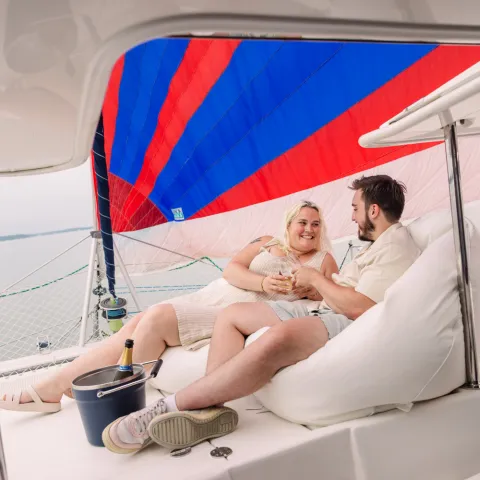 Couple relaxing on a boat with a sailing backdrop.