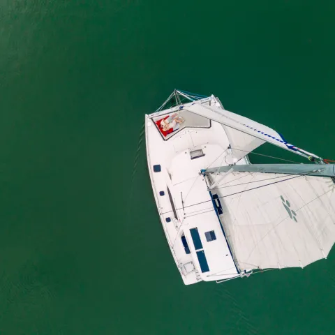 Aerial view of a white sailboat with two sails on green water.