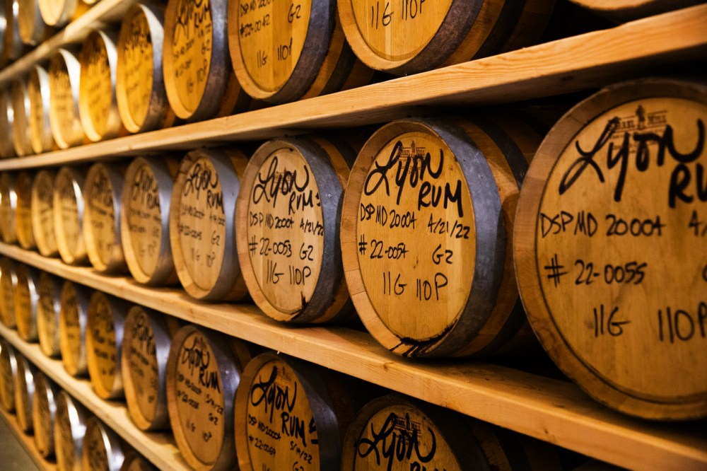 Stacked wooden barrels labeled 'Lyon Rum' in a dimly lit storage cellar.