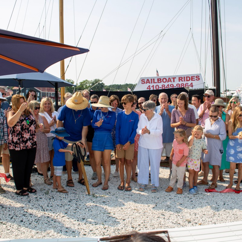 Group of people gathered outdoors by sailboats on a sunny day.