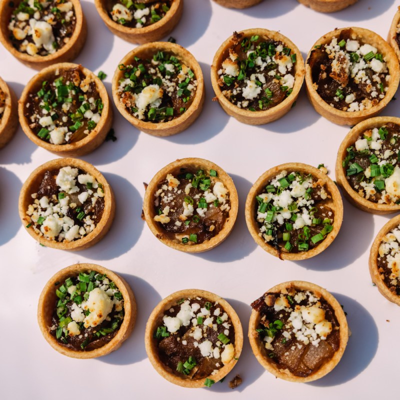 Mini tartlets with savory toppings on a white background.