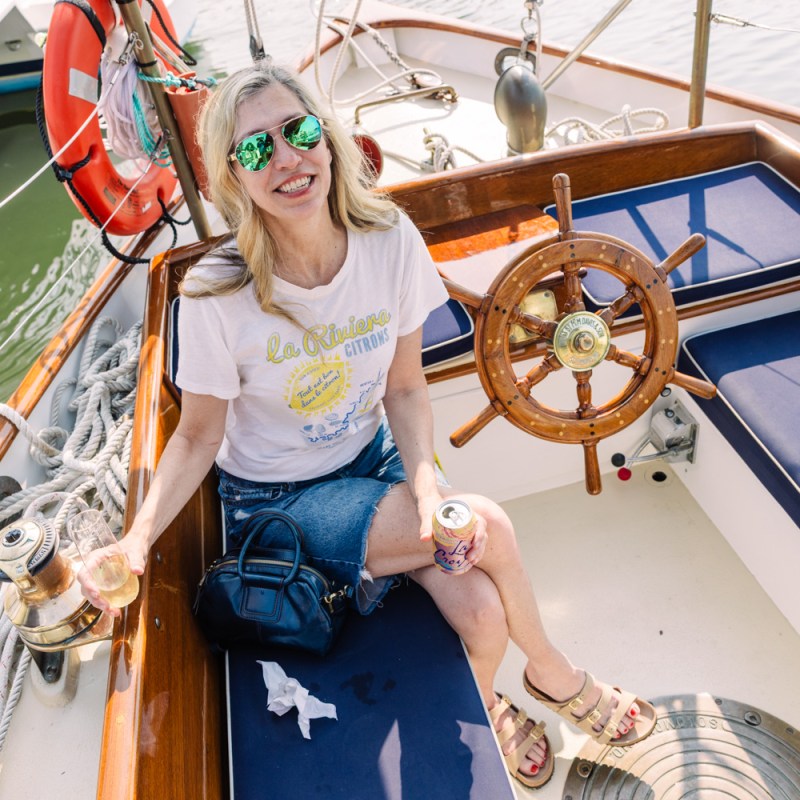 Woman smiling on a boat, wearing sunglasses, holding a drink.