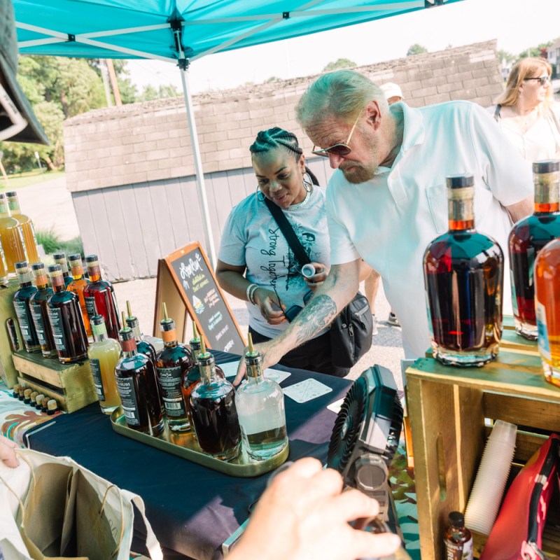 People examining bottles at an outdoor market stall with alcoholic beverages.