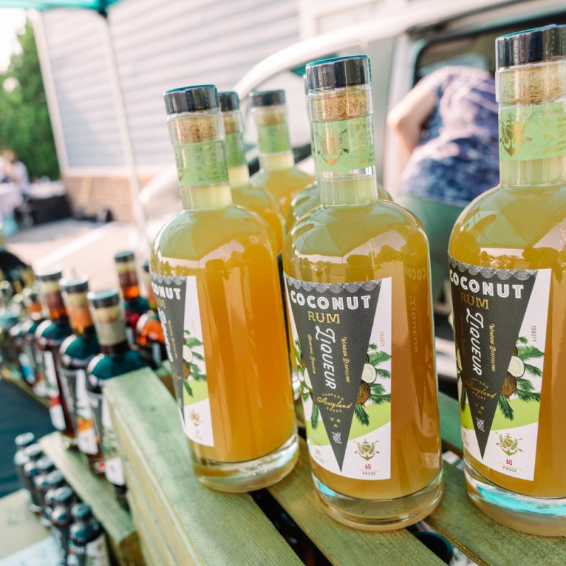 Three bottles of coconut liqueur on a wooden table at an outdoor market.