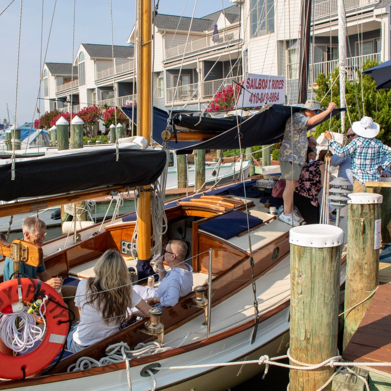 People boarding a sailboat docked near waterfront buildings.