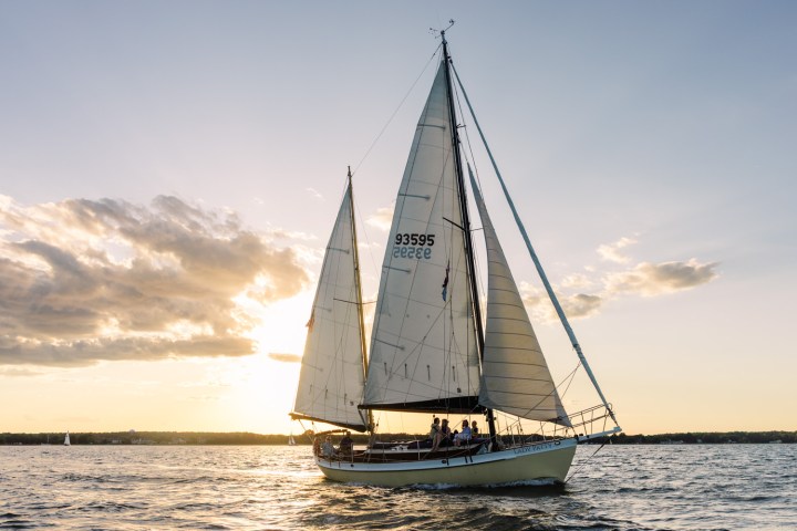 Sailboat on water at sunset with clouds and horizon.